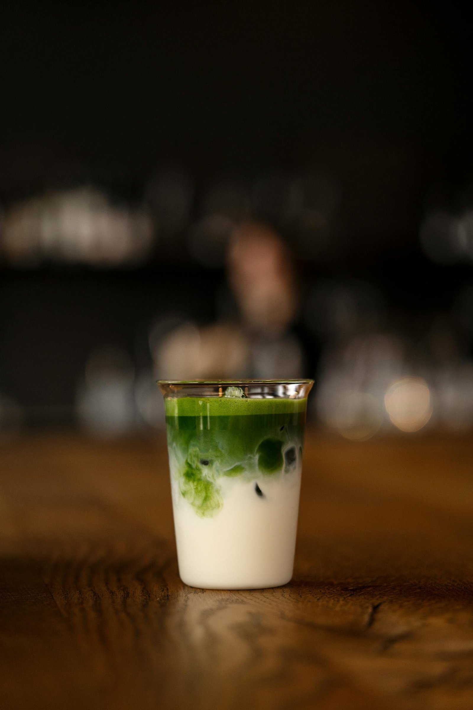 Elegant glass of matcha latte on wooden table, featuring layers of vibrant green matcha and creamy milk.