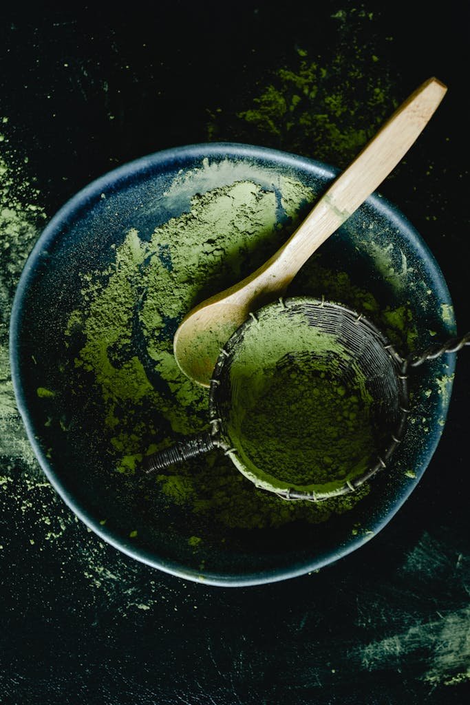 Overhead view of green matcha powder with a wooden spoon in a dark blue ceramic bowl