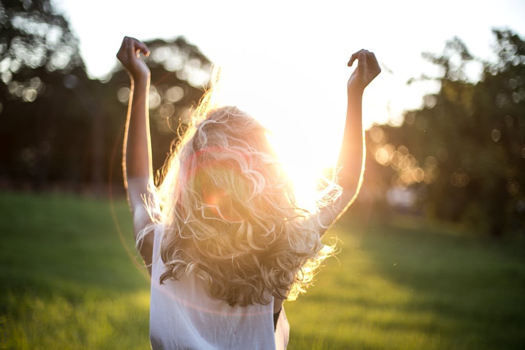 Thé matcha bienfaits cheveux : cela rend-il les cheveux plus longs? 9 A woman with outstretched arms celebrates the sunset in a grassy field, capturing the essence of freedom and joy.